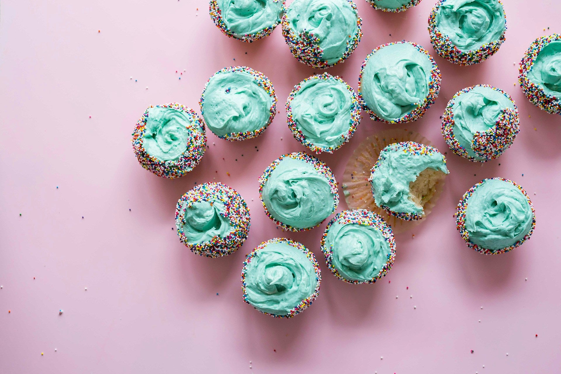Cupcakes with green icing on a pink surface.