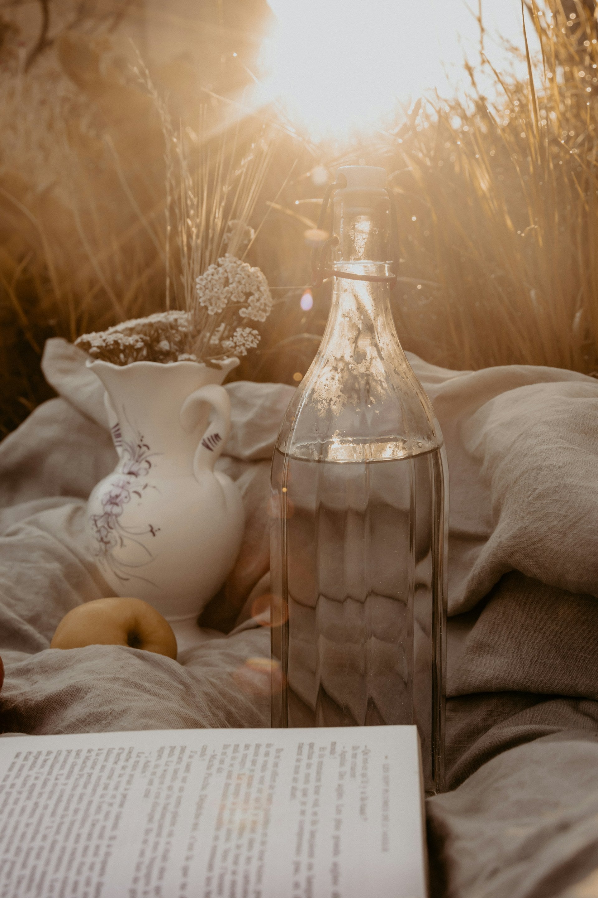 A vessel of water beside a book on a blanket outside.