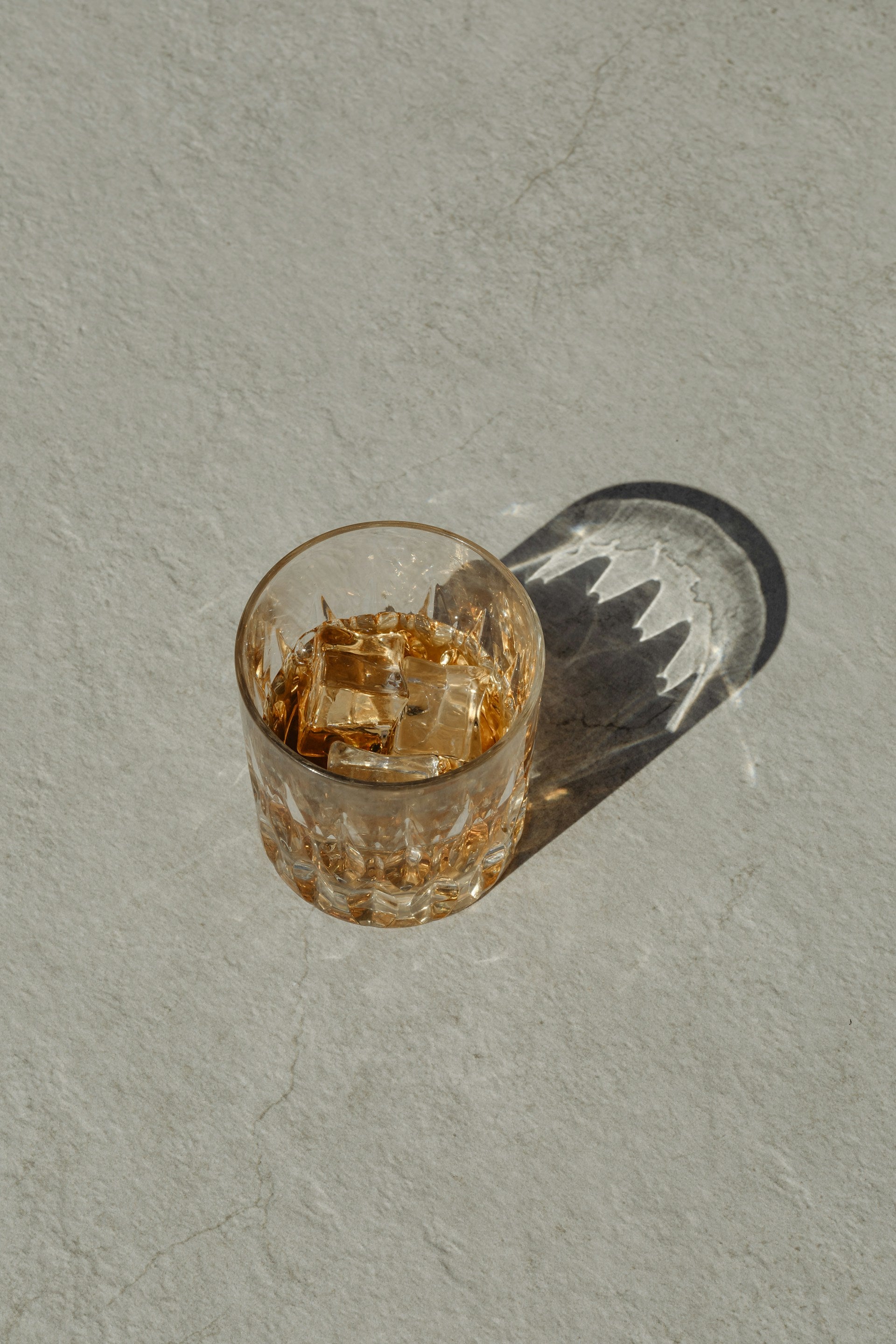 A glass of whiskey sitting on top of a concrete surface, with a reflection.