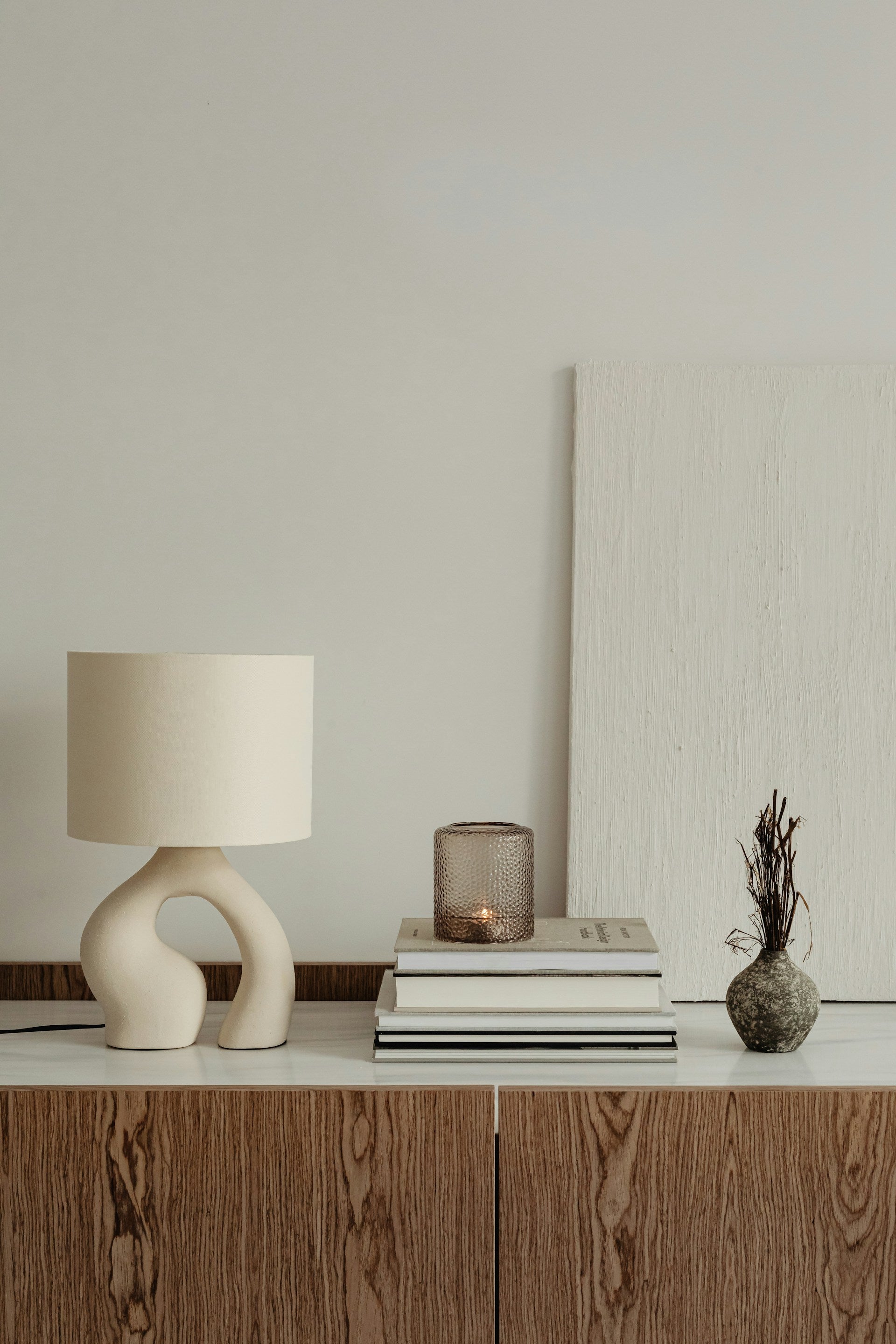 A table with a lamp, books and a vase on it.