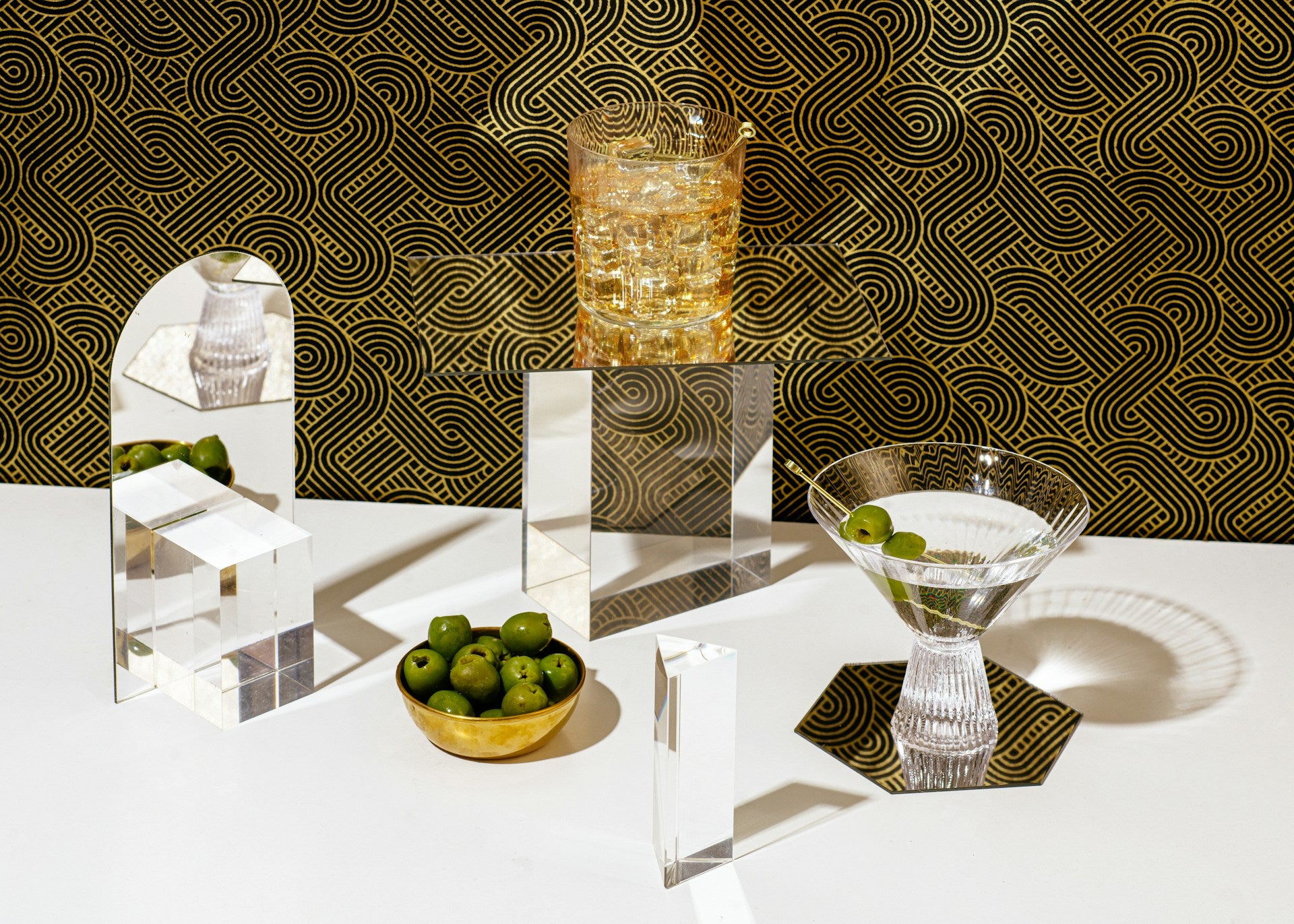 A white table with cocktails, a bowl of olives, and glass decorations.