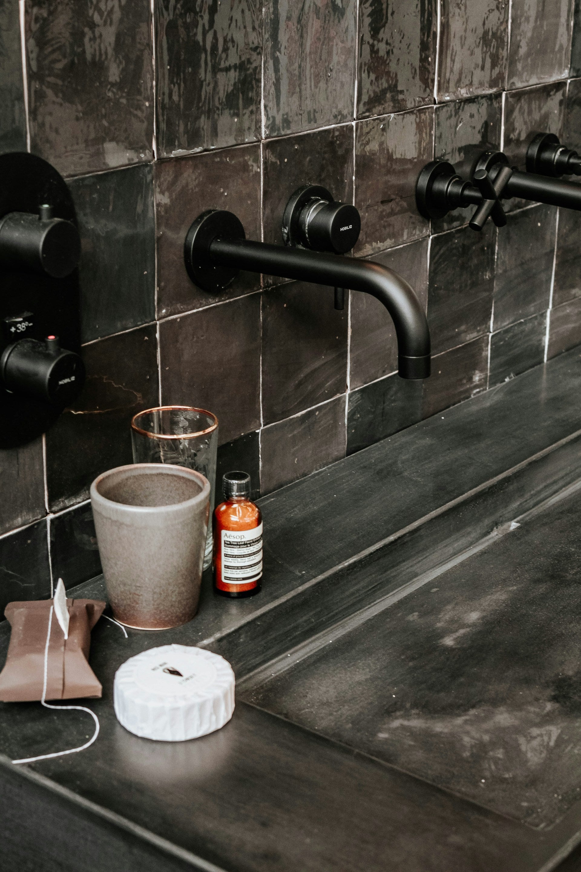 A sink with two faucets and a cup on the counter.
