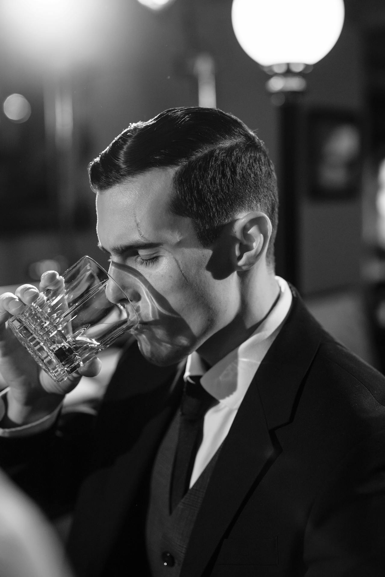 A person in a suit drinking out of a crystal glass, in black and white.