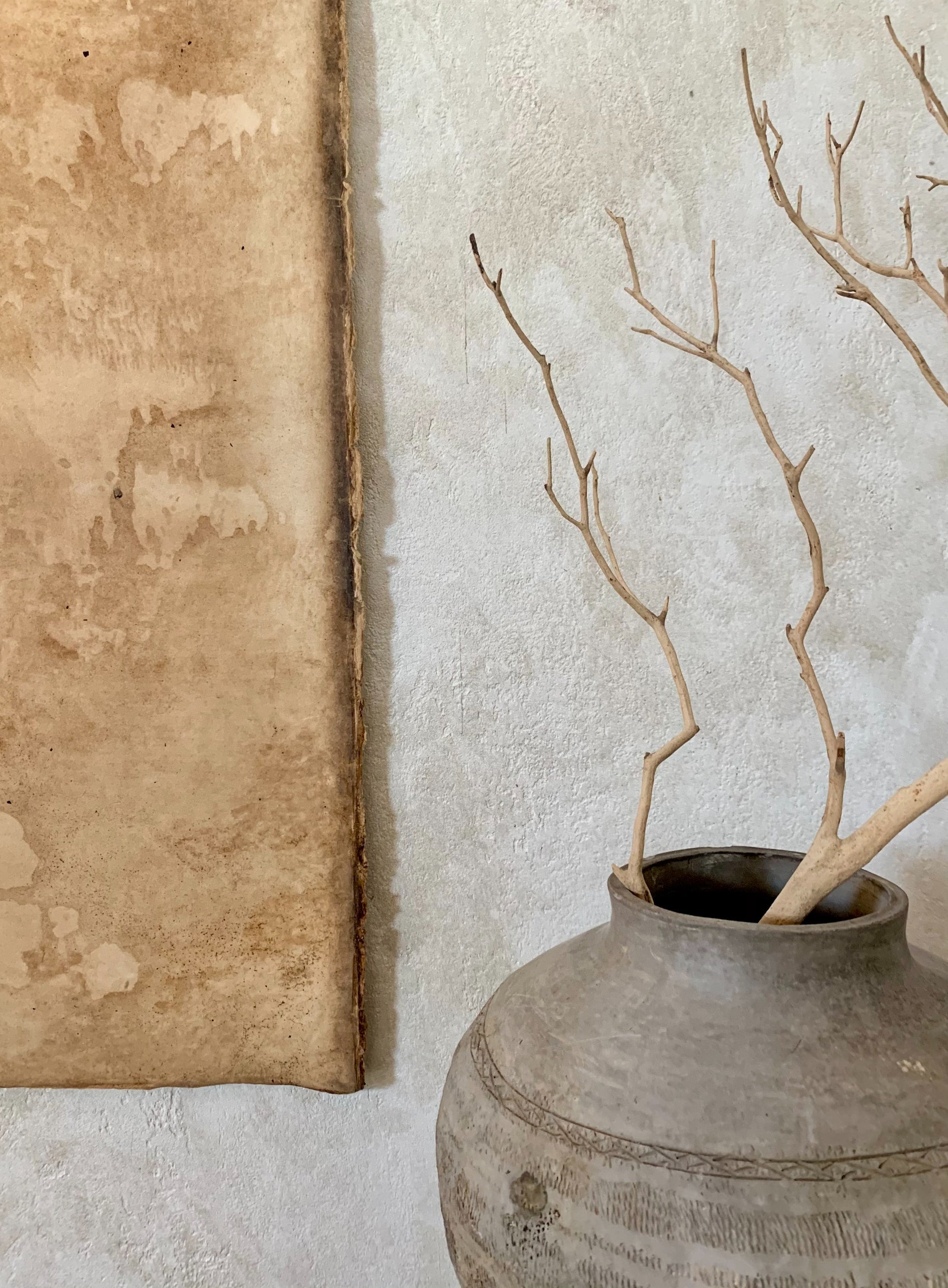 A vase with branches sitting beside a canvas.
