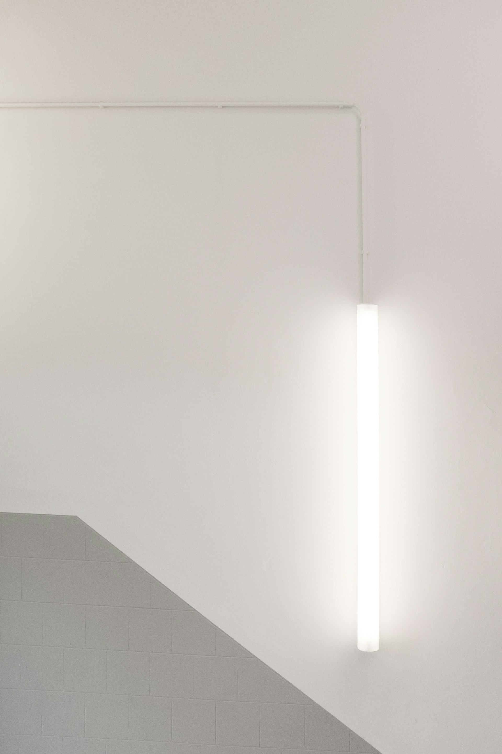 A white wall with a light fixture hanging from the ceiling.