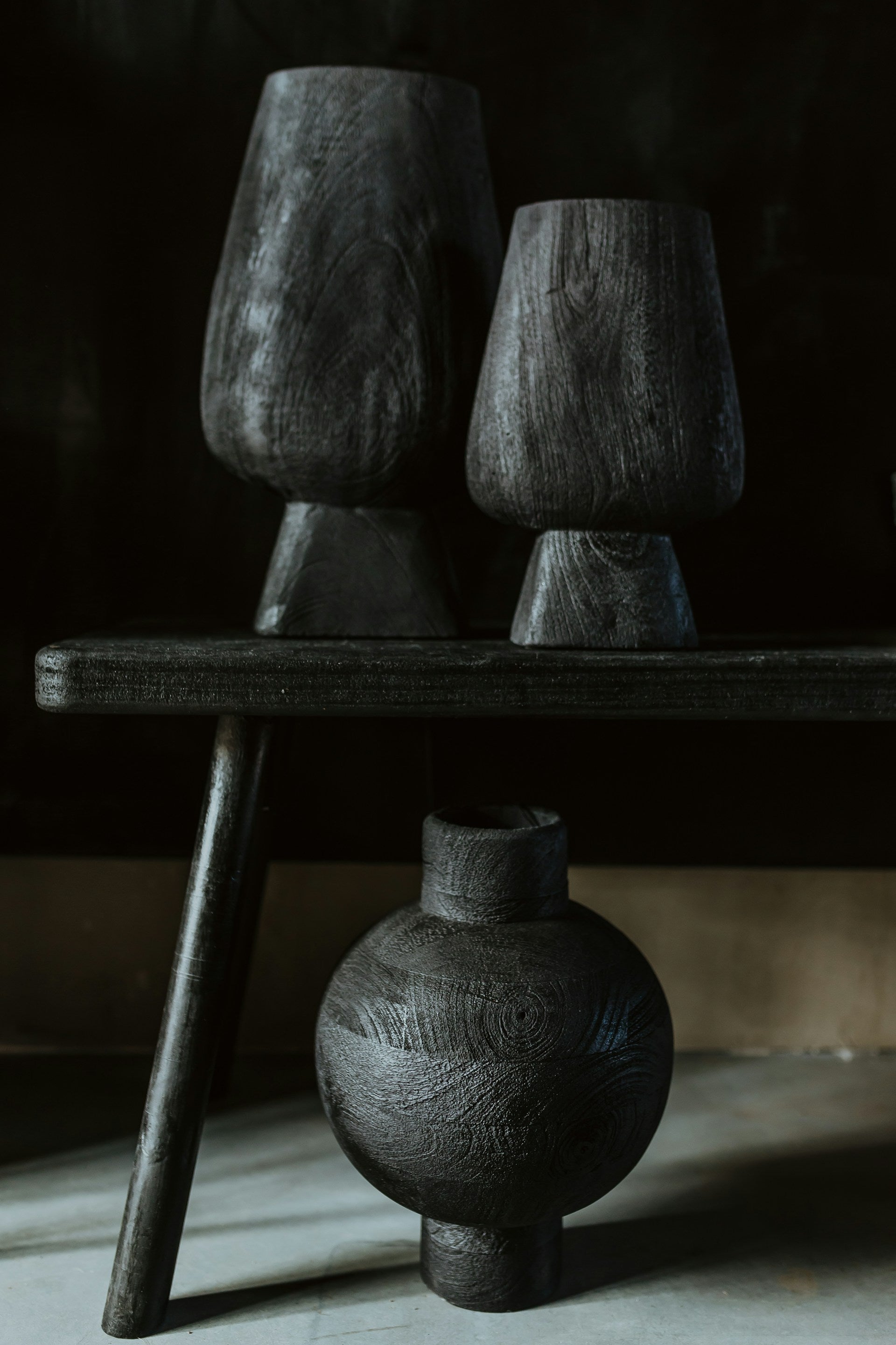 Three black vases, two are sitting on a wooden bench.