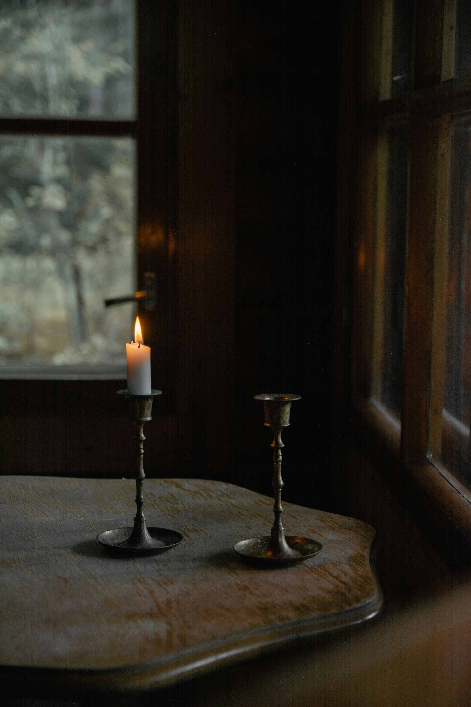 Two candles sitting on a table in front of a window.