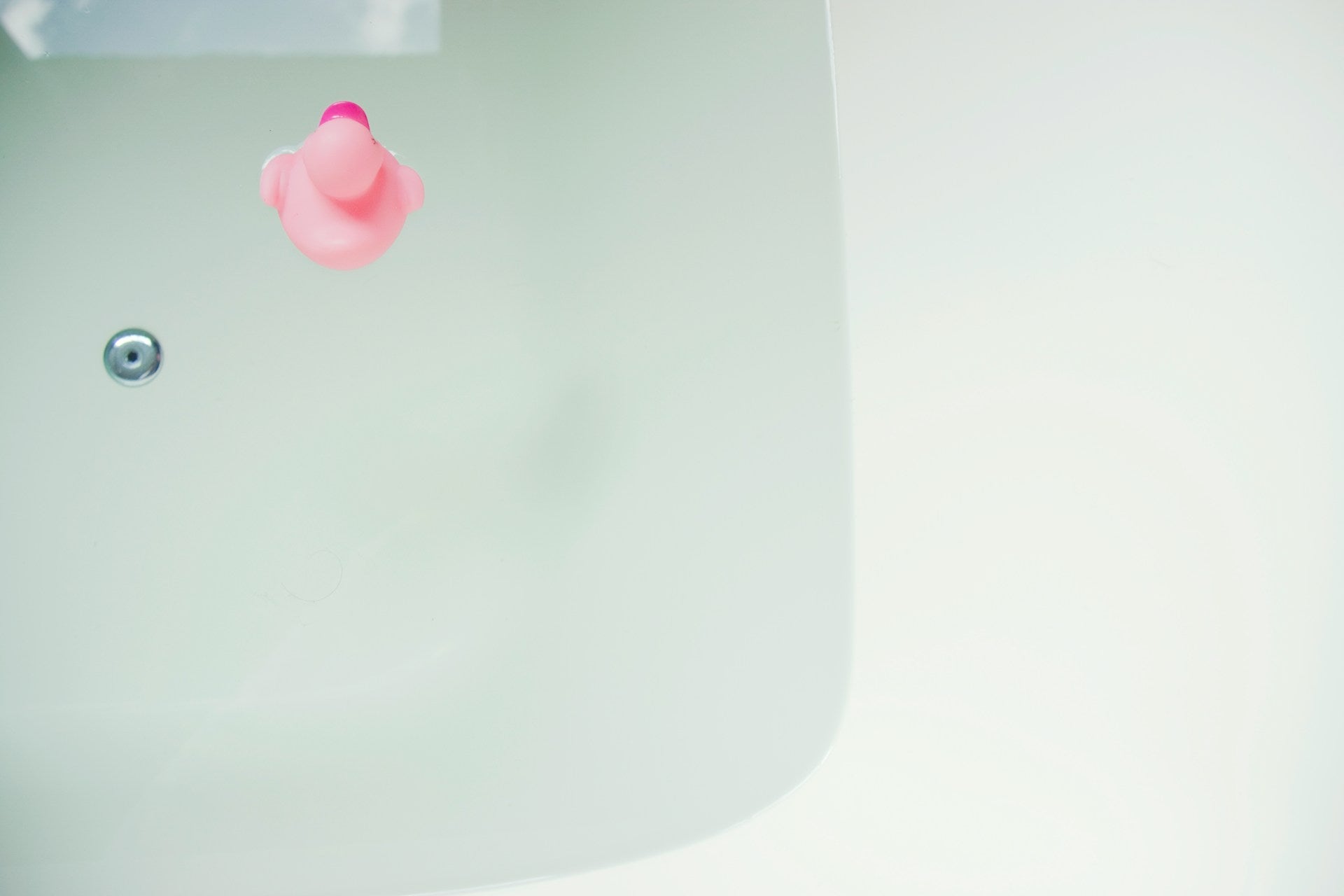 A bathtub of water with a pink rubber duck.