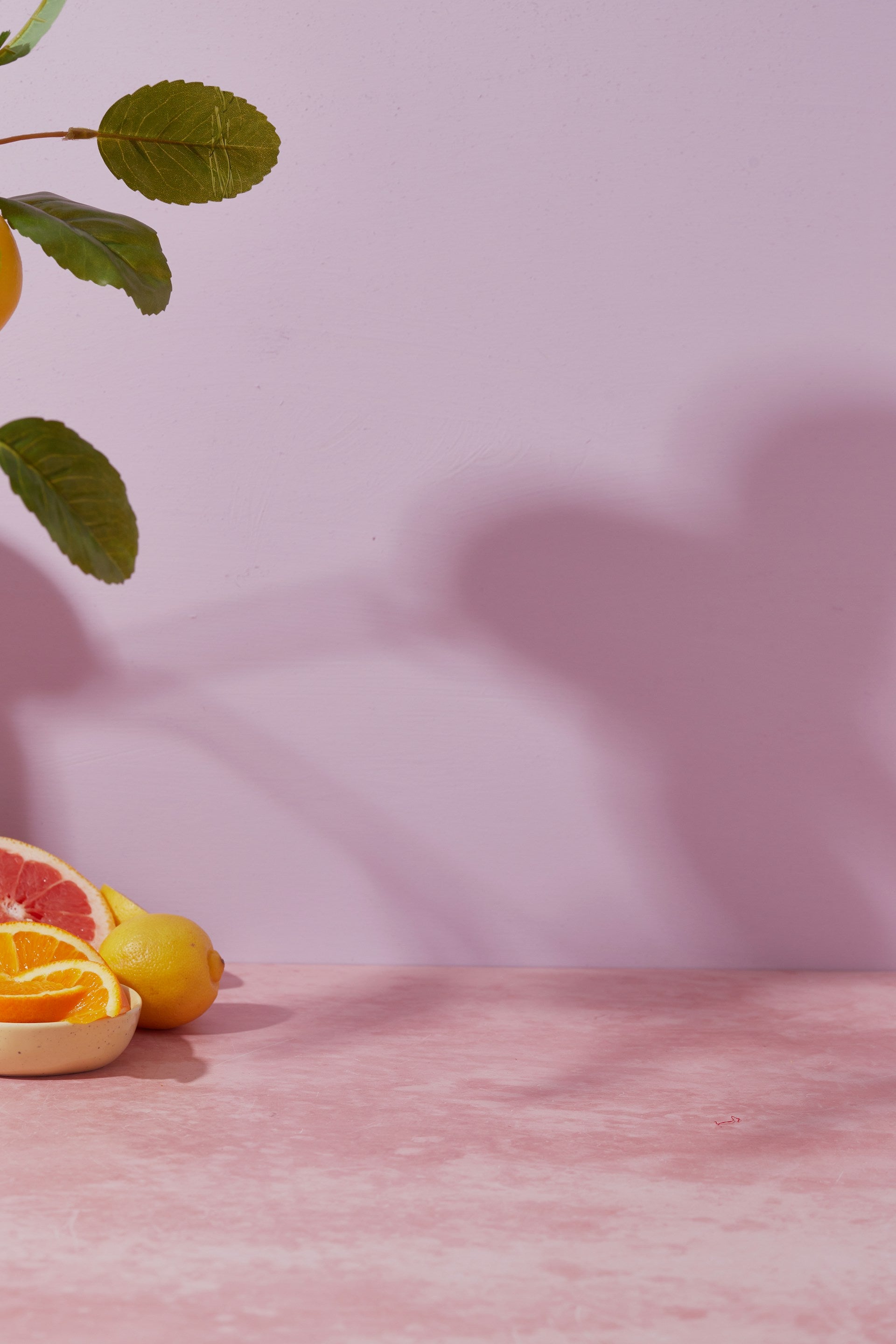 Citrus fruits and a shadow on a pink wall.