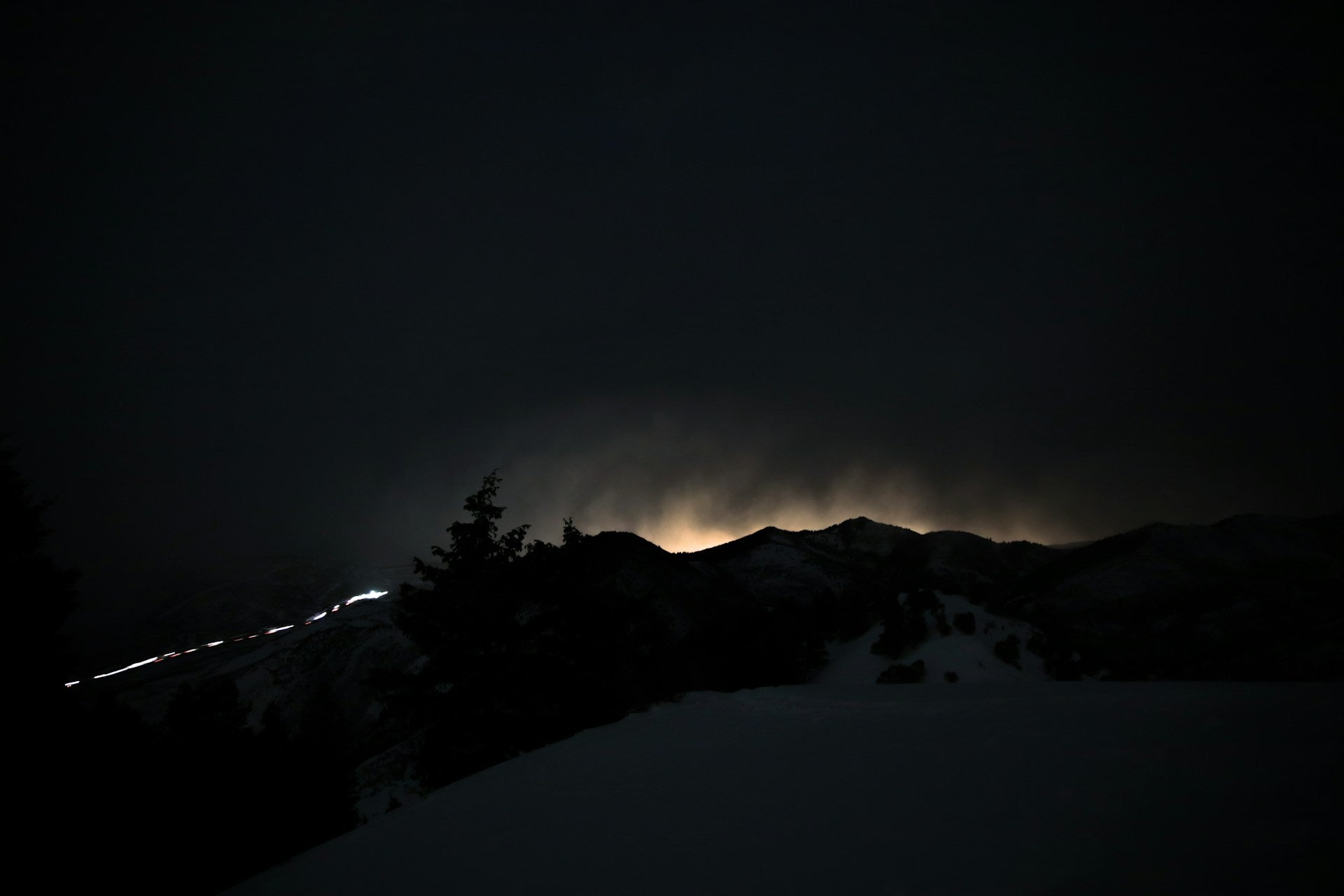A snow covered mountain at night with a light shining behind it.