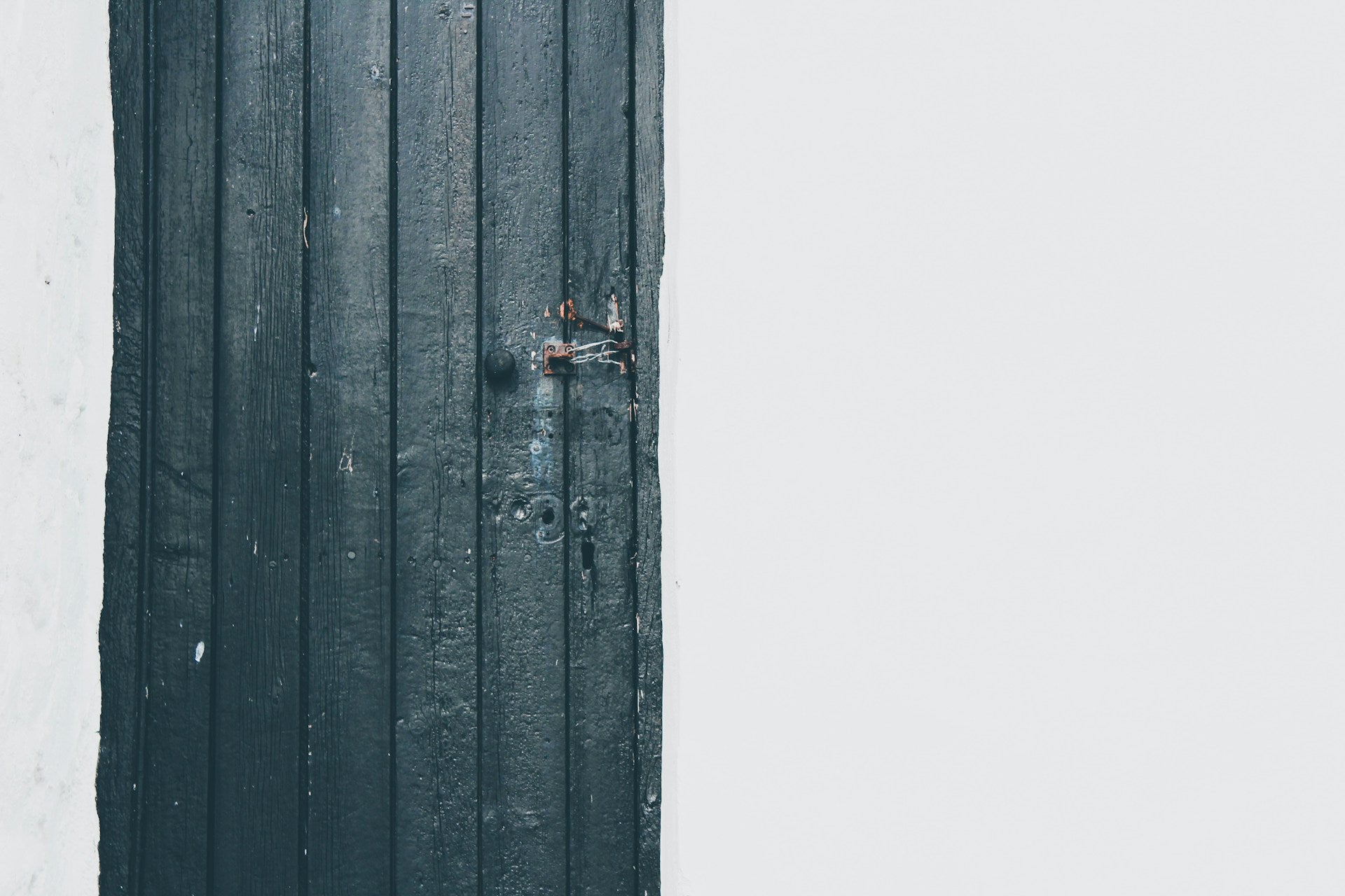 An old black wooden door with white walls.