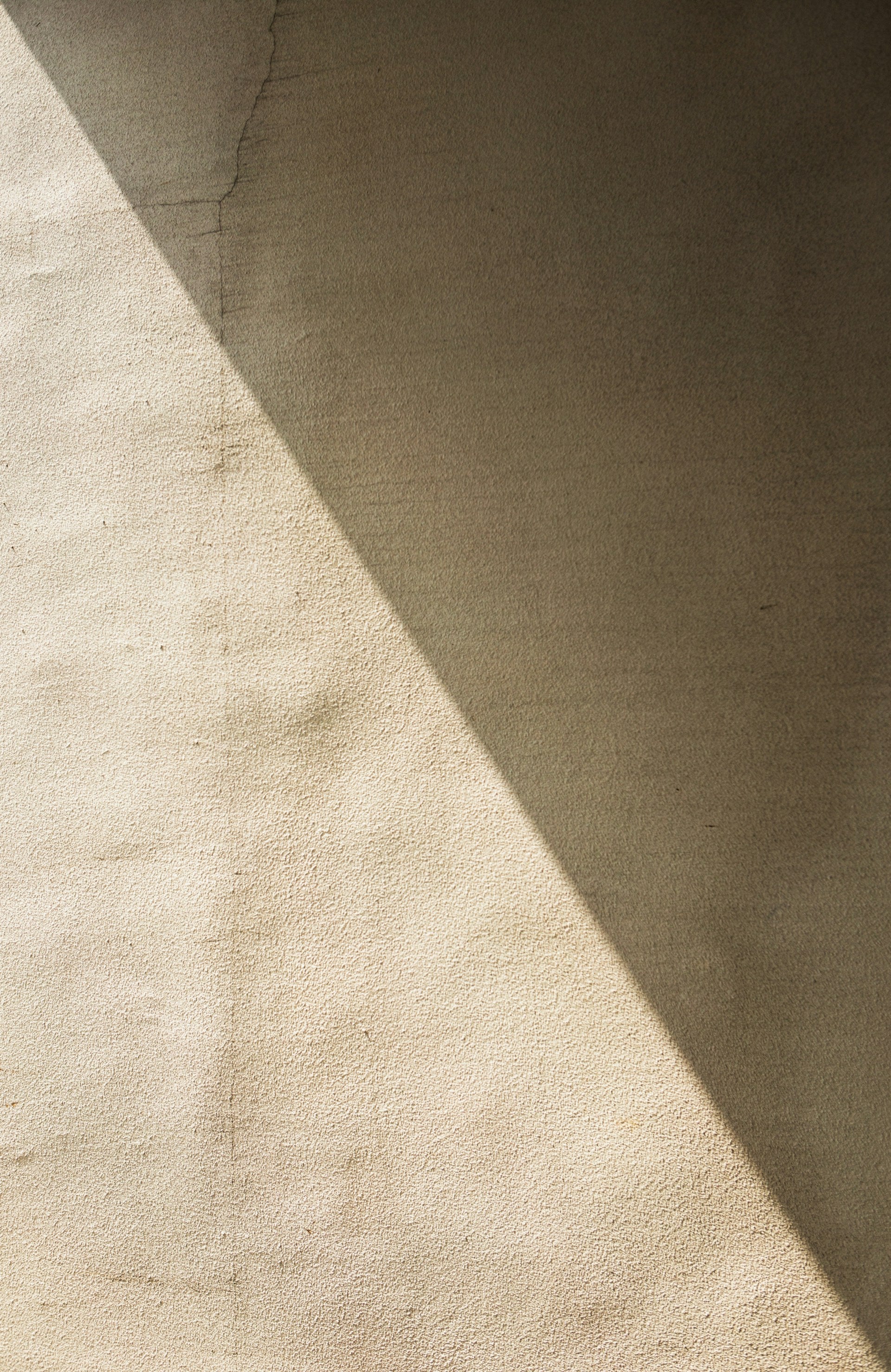 A diagonal shadow on a beige textured wall.